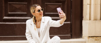 Frau in wei&szlig;em Hosenanzug und Brille macht ein Selfie