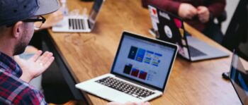 Mann mit Kappe sitzt mit Laptop in einem Meeting