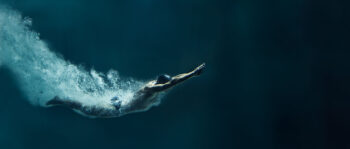 Mann mit Badehaube taucht in Wasser ein