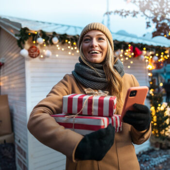 Frau h&auml;lt Geschenke und Smartphone in der Hand