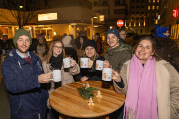 Gruppe um Stehtisch h&auml;lt Punschheferl in die Luft