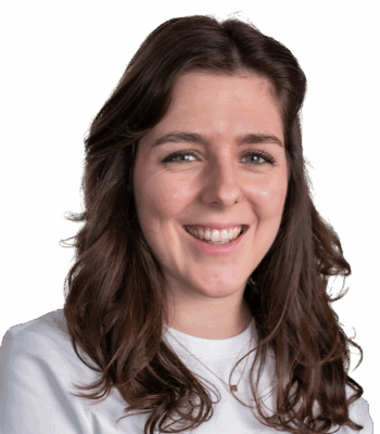 Eine Frau mit langen, gewellten braunen Haaren l&auml;chelt in die Kamera und verk&ouml;rpert Selbstvertrauen und Kreativit&auml;t - Qualit&auml;ten, die im Performance Marketing unerl&auml;sslich sind. Sie tr&auml;gt ein wei&szlig;es Oberteil und eine zarte Halskette vor einem hellgrauen Hintergrund.