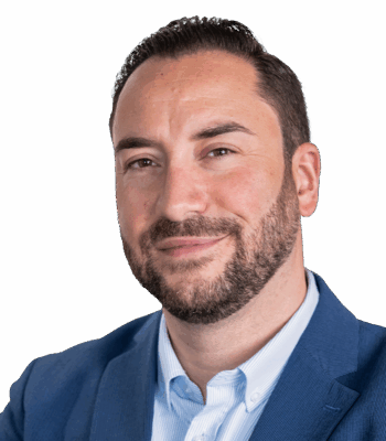 Ein Performance Manager mit kurzen dunklen Haaren und gestutztem Bart, der einen blauen Blazer &uuml;ber einem hellblauen Hemd tr&auml;gt, blickt leicht l&auml;chelnd in die Kamera vor einem schlichten hellen Hintergrund.