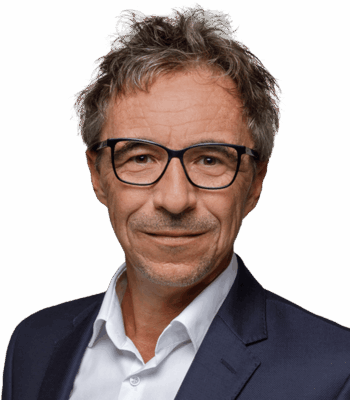 Ein Mann mittleren Alters mit kurzen, zerzausten grauen Haaren, der eine Brille, ein weißes Hemd und eine dunkle Anzugsjacke trägt, lächelt leicht vor einem schlichten weißen Hintergrund - und zeigt damit die selbstbewusste Präsenz eines KI-Beraters, der sich auf Strategie und Leistung konzentriert.